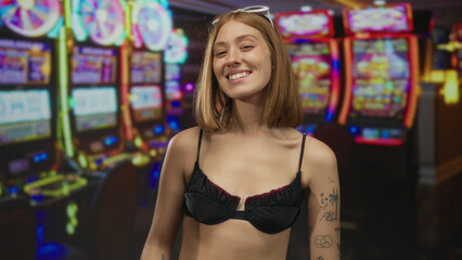 Young blonde woman smiling indoors at a casino with colorful slot machines in the background.