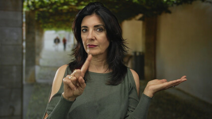 Woman shows serious face and finger pointing and open palm gesture on street; defiance.