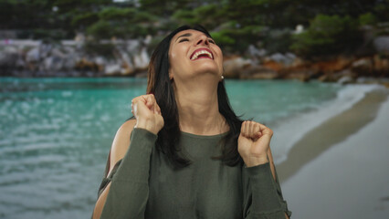 Middleaged hispanic woman raising clenched fists and smiling in studio; celebration joy empowerment...