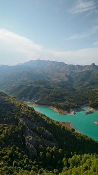 Drone video of the turquoise Guadalest Reservoir in Spain, surrounded by green hills and mountains, showing vivid water colors and scenic Mediterranean landscapes.