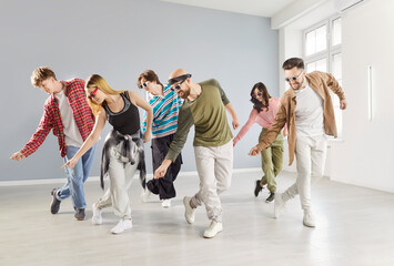 Group of joyful young adults in casual wear practicing dynamic choreography together in dance studio. Energetic dancers moving in sync while enjoying modern and hip hop session during group class.