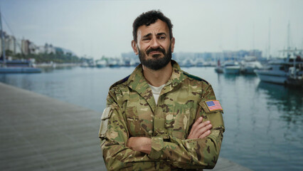 Military man with beard in uniform stands at a bustling port with ships and boats in the...