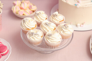 Dessert stand with tasty white cupcakes and other sweets for birthday party on pink table