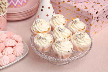 Dessert stand with tasty white cupcakes, gift and other sweets for birthday party on pink table