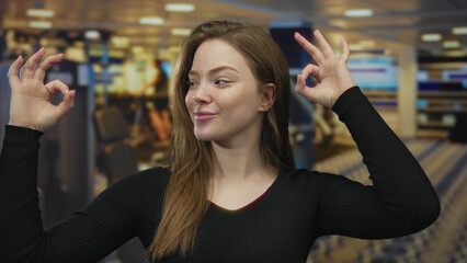 Young caucasian woman makes ok sign with both hands in a gym building surrounded by blurred workout...