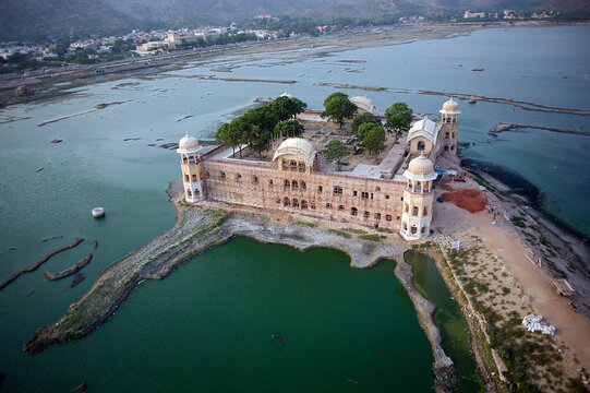 Aerial view of Jal Mahal's sandstone walls emerging from the tranquil waters of Man Sagar Lake, a serene jewel amidst the rugged landscape, Jaipur, Rajasthan, India.