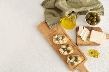 Wooden board of bread slices with tasty feta cheese and olives on white background
