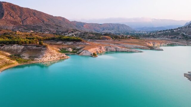 Drone video showing turquoise waters and rocky shoreline in Spain, with golden hour sunlight highlighting the rugged cliffs and surrounding landscape.