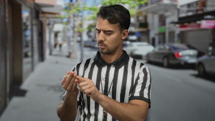 Young hispanic man referee on city street counting fingers thoughtfully while standing in outdoor...