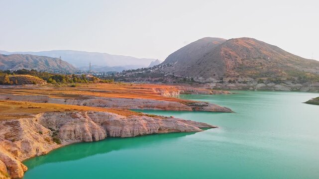 Drone video showing a sharp rocky peninsula surrounded by vibrant turquoise waters of a Spanish lake, bathed in warm golden hour sunlight.