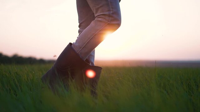 Walking through tall grass at sunset boot and jean clad leg step through green field with sun low on horizon flare catching boot edge nature and slow walking pace under warm evening light glow