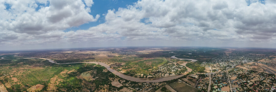 Aerial view of the Tana river snaking through the green landscape and sandy terrain under a vast sky, Garissa, Kenya.