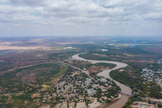 Aerial view of the Tana river snaking through the parched landscape, cutting through the sparse green vegetation and infrastructure, Garissa, Kenya.