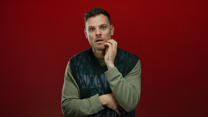 Young man posing confidently against an isolated red background, radiating charm with a thoughtful expression and casual attire embracing modern style and elegance.