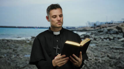 Clergyman reading at the rocky beach with an open book, capturing the serene seaside atmosphere.