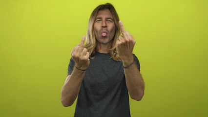 Blond man with long hair sticks tongue out and flips both middle fingers in a studio setting;...