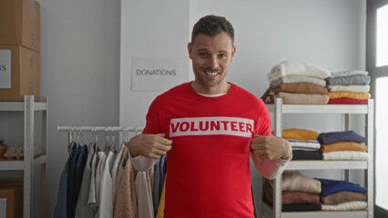 Young man in red volunteer shirt points and gives thumbs up indoors at a donation center surrounded...