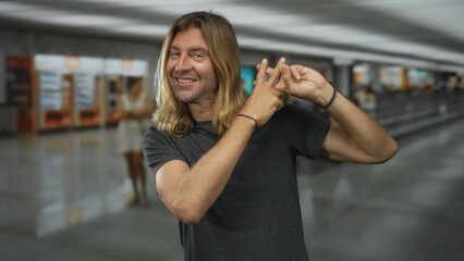 Fototapeta premium Man with long hair in dark grey shirt makes hashtag gesture with fingers at airport terminal; playful connection.