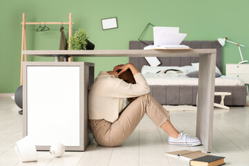 Woman hiding under table during earthquake in bedroom