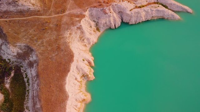 Drone video captures a rocky shoreline with green vegetation surrounded by bright turquoise waters of a lake in Spain, viewed directly from above.