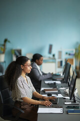 Young adult biracial woman working at computer in modern office, sitting at desk with hands on...