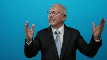 Senior business man gestures passionately against a vibrant blue background wearing a suit and...