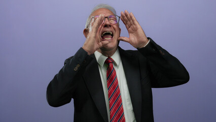Senior man in business suit shouting energetically against an isolated purple background wall,...