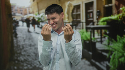 Man in light shirt showing hand gesture of spending money on old town street with cobblestone path...