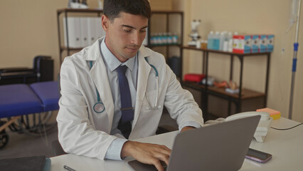 Man doctor in white coat typing on laptop with stethoscope around neck in hospital clinic; professionalism.