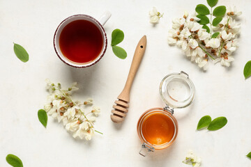 Jar of sweet honey with acacia flowers and cup of tea on white background