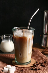 Glass of iced latte with coffee beans and cubes of sugar on wooden table