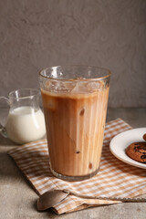 Glass of iced latte and jug of milk on grey background