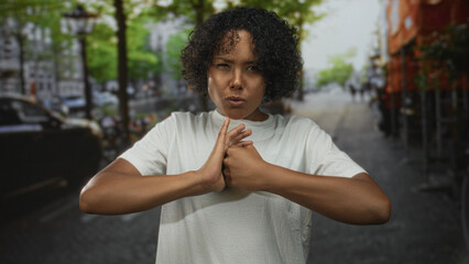 Young african american woman presses hands together in a focused gesture on a city street;...