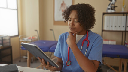 Woman doctor examines tablet with hand on chin and draped red stethoscope in bright clinic...