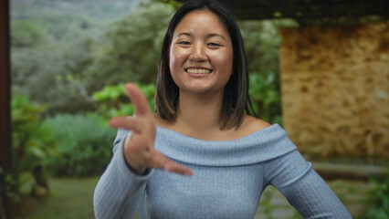 Woman smiling in a park with outstretched hand wearing blue sweater outdoor surrounded by greenery...