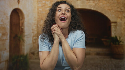 Hispanic woman clasping hands in front of weathered stone arch on old town street under warm...
