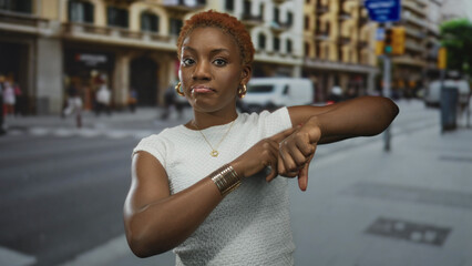 Woman in a white top points finger to her wrist on a busy city street near a traffic light and...