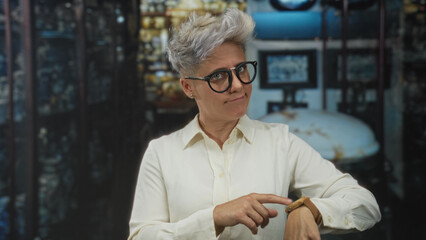 Caucasian woman with short hair wearing glasses pointing finger to watch and checking time in...