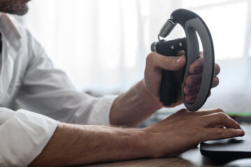 Male employee squeezing black hand gripper while working on computer. Close-up of hand training...