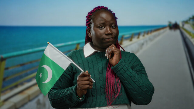 Woman holding pakistan flag standing on seaside promenade with ocean backdrop expressing diversity and cross-cultural connection through travel and tourism outdoors.