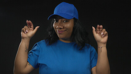 Woman hands making air quotes in studio wearing blue cap and shirt with subtle smile and raised eyebrows; playful sarcasm.