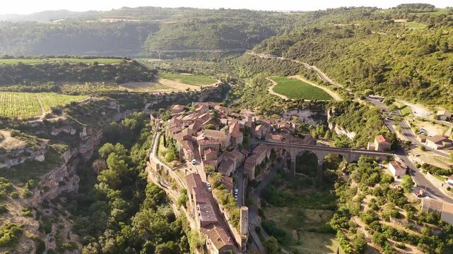 Aerial view of the ancient Minerve village with its bridge, nestled in a valley with contrasting green trees and red-tiled roofs, Minerve, Occitanie, France.