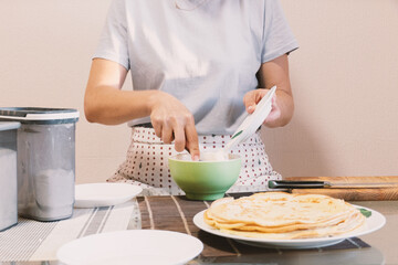A person in an apron prepares ingredients in a bowl for a homemade meal, with a stack of delicious pancakes ready on the table. Perfect for food, cooking, and home lifestyle themes.