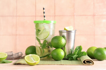 Glass of fresh Mojito cocktail with limes and mint on beige table