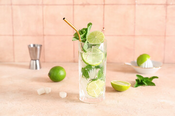 Glass of fresh Mojito cocktail with limes and mint on beige table