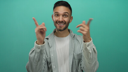 Fototapeta premium Young hispanic man pointing to his smile with both hands against a bright blue background, expressing happiness and confidence.