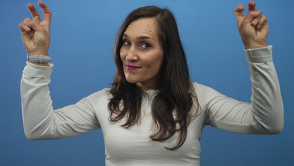 Young hispanic woman makes air quotes gesture with fingers against a blue studio wall; sarcasm irony doubt.