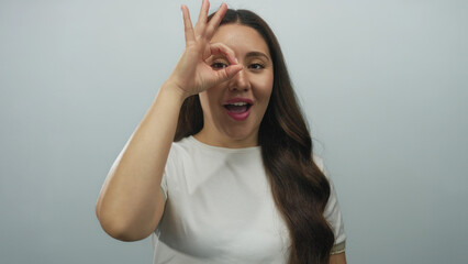 Smiling young hispanic woman shows ok sign in a pale blue studio setting with visible hand gesture;...