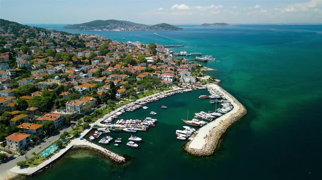 Aerial view of red-roofed buildings nestled amongst lush greenery and clear turquoise waters surrounding Buyukada Island, Princes' Islands, Istanbul, Turkey.