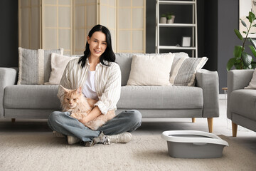 Beautiful young happy woman and cute Maine Coon cat with litter box sitting on floor at home